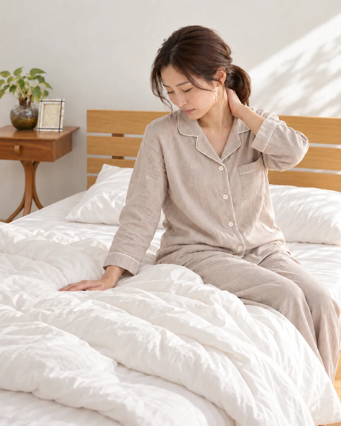 朝、ベッドの上で起き上がり、首の後ろに手をやる女性